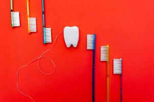 Six tooth brushes in raw near toy tooth. Red background. Dental concept. photo