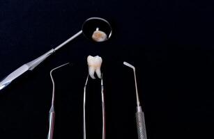 Dental instruments around ceramic tooth model. Black background. Art photo. photo