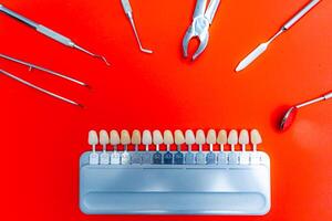 Color tone palette in the middle. Metal dental instruments around. Red background. photo