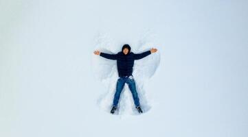 A young child playing in the snow making an angle. Boy plays in white snow. View from the top. photo