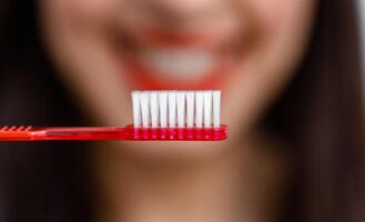 Smiling young woman with healthy teeth holds a toothbrush. Selective focus. Cropped photo. Blurred background. photo