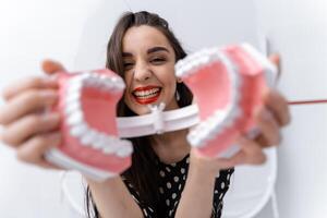 gracioso niña con un abrió dental mandíbula cerca rostro. mujer andando con el plastico educativo dientes modelo. foto