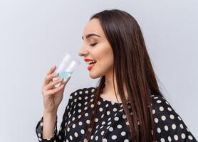 sano joven mujer con vaso de Fresco agua en blanco antecedentes. morena niña con rojo labios y largo cabello. foto