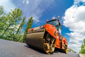 Road roller flattening new asphalt. Heavy vibration roller at work paving asphalt, road repairing. Selective focus. photo