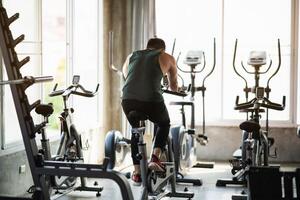 Back view. Asian sportsman exercising on a bicycle in the gym, determination to cardio lose weight, makes her healthy. exercise bike man fitness sport concept. photo