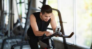 Asian sportsman exercising on a bicycle in the gym, determination to cardio lose weight, makes her healthy. exercise bike man fitness sport concept. photo