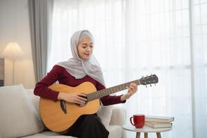 musulmán islam mujer vistiendo hijab o gris bufanda es jugando un guitarra. ella es sonriente y ella es disfrutando sí misma foto