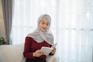 Muslim Islam woman wearing hijab or grey scarf is reading a book. She is smiling and she is enjoying her reading photo