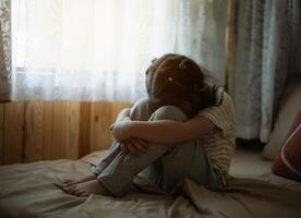 silueta Deprimido niña es sentado en un cama con su cabeza abajo. ella es llanto. escena es triste y emocional. depresión salud concepto. foto