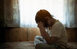 Silhouette depressed young girl is sitting on a bed and crying. She is wearing a striped shirt and has her hands on her head. Depression health concept. photo