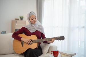 musulmán islam mujer vistiendo hijab o gris bufanda es jugando un guitarra. ella es sonriente y ella es disfrutando sí misma foto