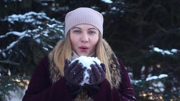 portret. een mooi gelukkig meisje in een licht hoed slagen sneeuw van haar handen in de Open lucht in winter hebben een mooi zo breken omhoog en glimlachen video