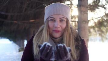 un hermosa niña en un sombrero disfruta naturaleza y golpes nieve desde su manos teniendo un bueno estado animico en el brillante clima video