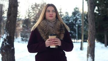 retrato. jovem lindo menina é caminhando dentro a parque ao ar livre dentro inverno dentro a parque e bebendo café video