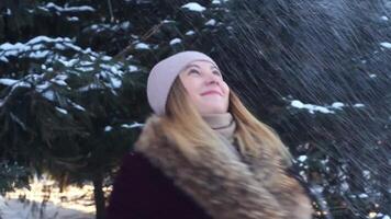 hermosa contento niña en un sombrero lanza nieve y remolinos en el abierto aire en el bosque video