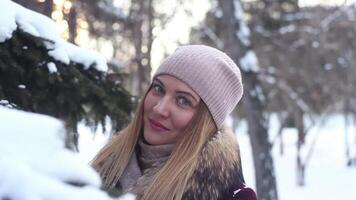 Portrait. Beautiful girl in a light hat stands in winter sunny weather in a forest near a tree and smiles video