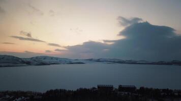 frostig damm med snö i mörk vit vinter- dag nära små stad. stock antal fot. antenn se av kväll solnedgång landskap av isig damm omgiven förbi bergen på molnig himmel bakgrund. video