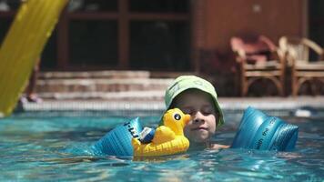 wenig Junge im Panama schwimmt mit aufblasbar Spielzeuge im das Schwimmbad auf ein sonnig Tag video