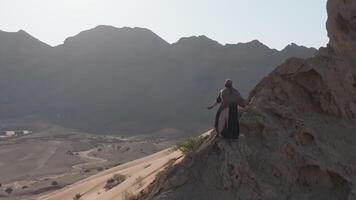 ein Mann mit ein Mitarbeiter im seine Hand und das Kleider von ein Schamane steht auf ein Felsen unter das Sand von das Wüste und Tänze video