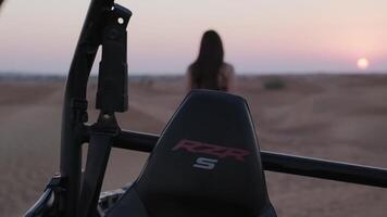 uma jovem mulher dentro uma fato de treino anda em longe a partir de uma buggy em pé dentro a deserto para a configuração Sol video