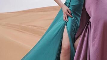 Two young women in long dresses developing in the wind stand barefoot through the sand dunes of the desert video