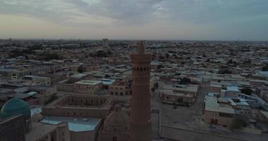 a zangão moscas por aí a minarete do a arquitetônico complexo poi-kalon. dentro a fundo estão a velho casas do bucara, uzbequistão. cedo nublado manhã video