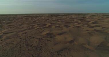 uma zangão moscas sobre uma homem dentro árabe roupas caminhando em a areia dunas do a deserto em a fundo do a pôr do sol video