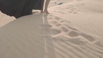 Young woman with long hair in a chic black dress stands barefoot on the desert sand video