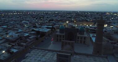 A drone flies over the architectural complex Poi-Kalon among old houses in Bukhara, Uzbekistan. Cloudy night video