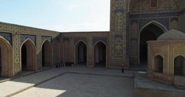 de Drönare flugor runt om de gård av de gammal komplex lyab-i hauz med turister på Det. gammal bukhara, uzbekistan. video