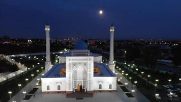 un zumbido moscas terminado un complejo de iluminado mezquita edificios a noche. nublado cielo en el antecedentes. video