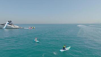 Dubai, UAE - 3 20 2023. A drone flies over a pair of young people sailing on SUP boards on the sea next to a private yacht video