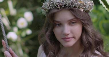 Jeune fille dans une couronne de fleurs oscillations sur balançoire video