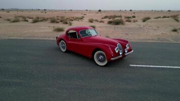 uma zangão moscas por aí a caro vermelho vintage carro em pé em a esvaziar estrada dentro a meio do uma arenoso deserto video