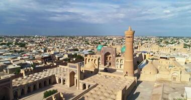 em uma ensolarado nublado dia, uma zangão moscas por aí a antigo torre do a complexo Kalyan minarete. velho bucara, uzbequistão. video