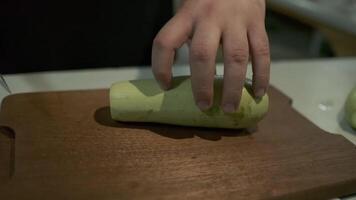 The chef cuts large pieces of zucchini with a knife on a cutting board. video