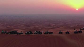 un' fuco mosche al di sopra di atvs in piedi su il sabbia dune di il deserto contro il fondale di il tramonto video