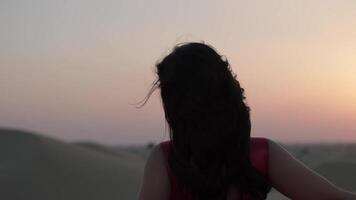 Young woman with black hair standing barefoot in a long red evening dress on the sand dunes of the desert video