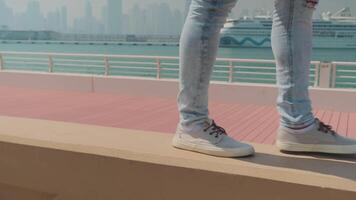 dubai, uae - 1 14 2022. en ung man i jeans, gymnastikskor och en vit t-shirt promenader längs de parapet längs de vägbank video