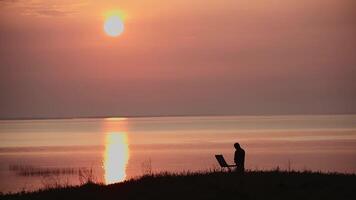 Silhouette of an artist with an easel on the bank of the river against the background of the sunset. video