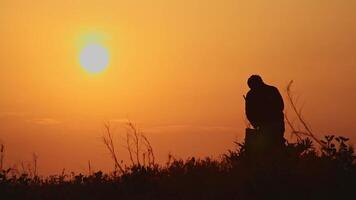 Silhouette of an artist with an easel on the bank of the river against the background of the sun. video