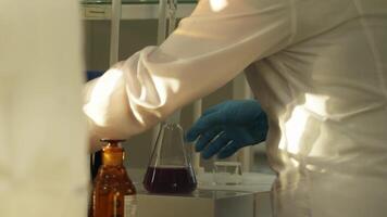 Hands of laboratory technician in protective clothing working with glassware in laboratory. video