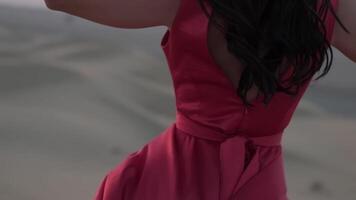 Young woman with black hair standing barefoot in a long red evening dress on the sand dunes of the desert video