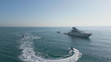 Dubai, UAE - 3 20 2023. A drone flies over people riding jet skis and an electric foil board on the sea around a yacht with Dubai in the backdrop video