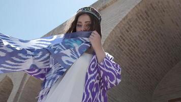 A young woman with long hair in an oriental robe and skullcap stands in the wind near an ancient mosque video