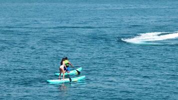 Dubai, UAE - 3 20 2023. A drone flies over a pair of young people sailing on SUP boards on the sea next to a private yacht video