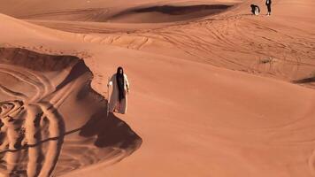 A man in shaman's clothes walks on the sand of the desert with a staff in his hands video