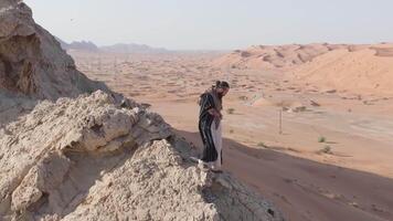 un hombre vestido como un chamán soportes en un rock en el medio de el Desierto y sostiene un móvil teléfono en su mano video