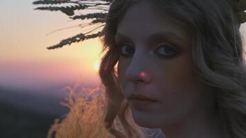 Close-up of the face of a young woman with bright makeup and in an autumn headdress against the background of the setting sun in the mountains video