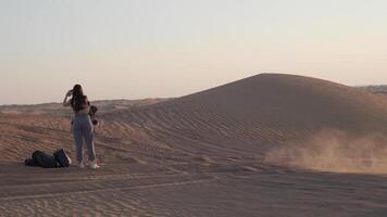 jovem mulher com grandes Preto cabelo dentro roupa de esporte em pé em deserto areia contra pôr do sol fundo video